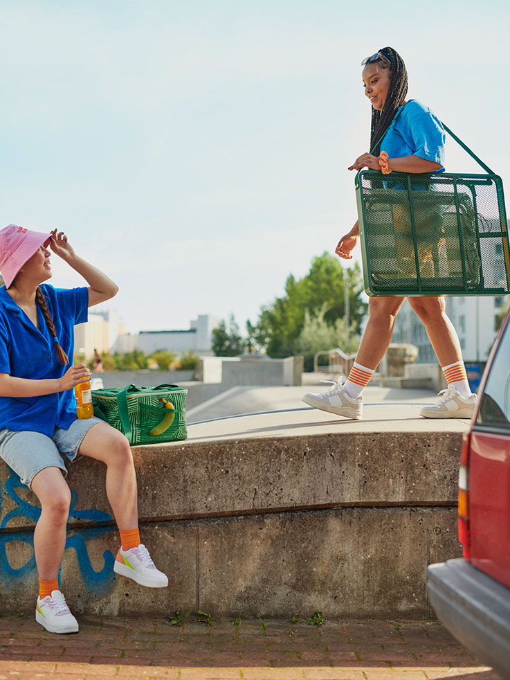 Young people sharing food at skate park. Green folding table and chair, orange cooler, relaxed vibe.