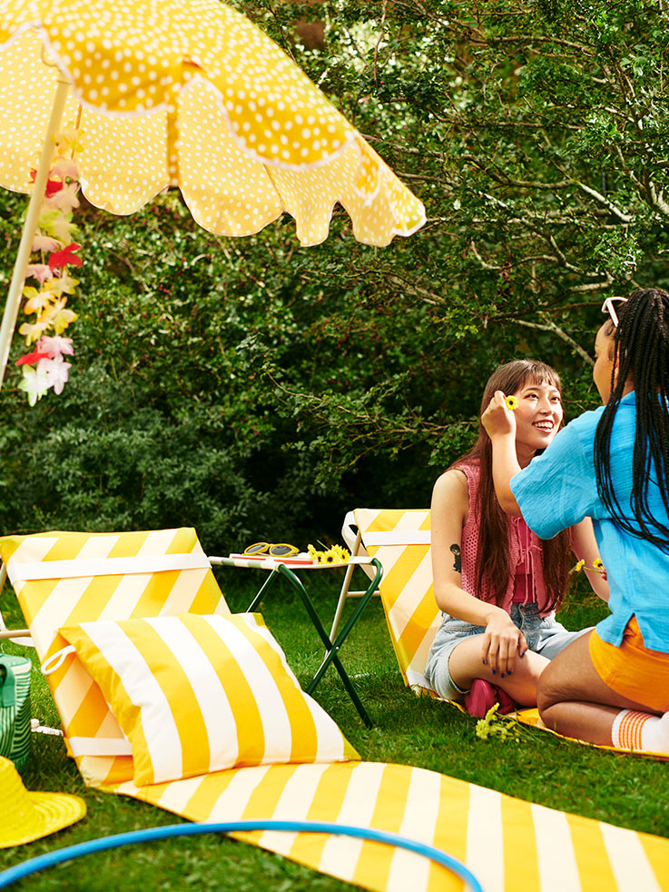 Friends under a yellow umbrella, with matching mats. Summer and cheerful garden atmosphere.