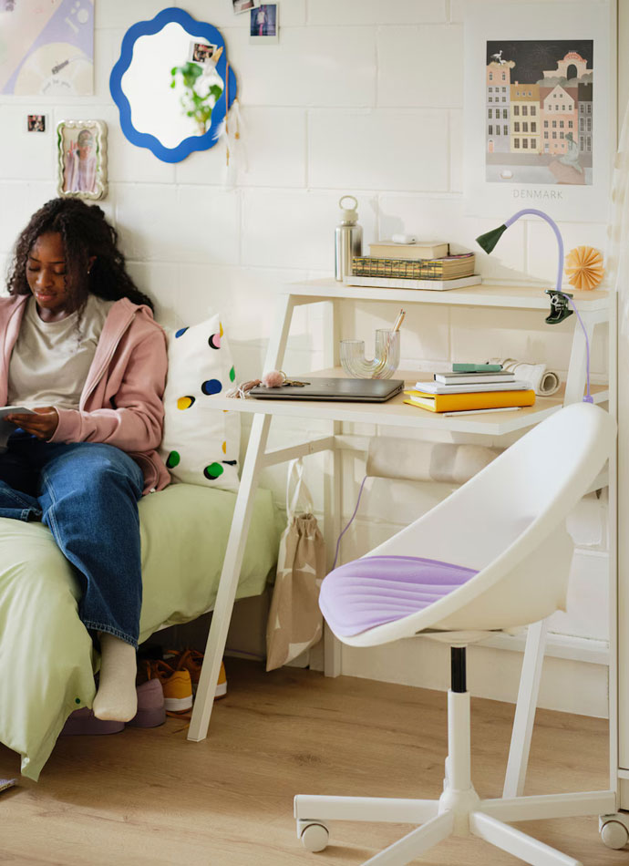 a creative style chair, in a student dormitory, in front of a modern and functional style desk on the side of the bed a girl seated