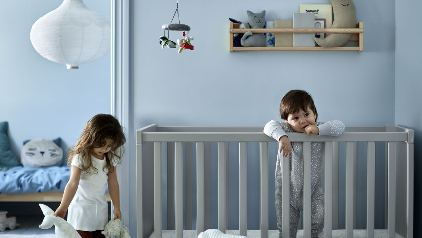 A baby in a SUNDVIK crib, a FLISAT wall storage, and a RISBYN pendant lamp.