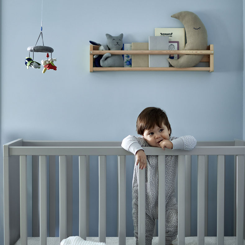 A baby in a SUNDVIK crib, a FLISAT wall storage, and a RISBYN pendant lamp.