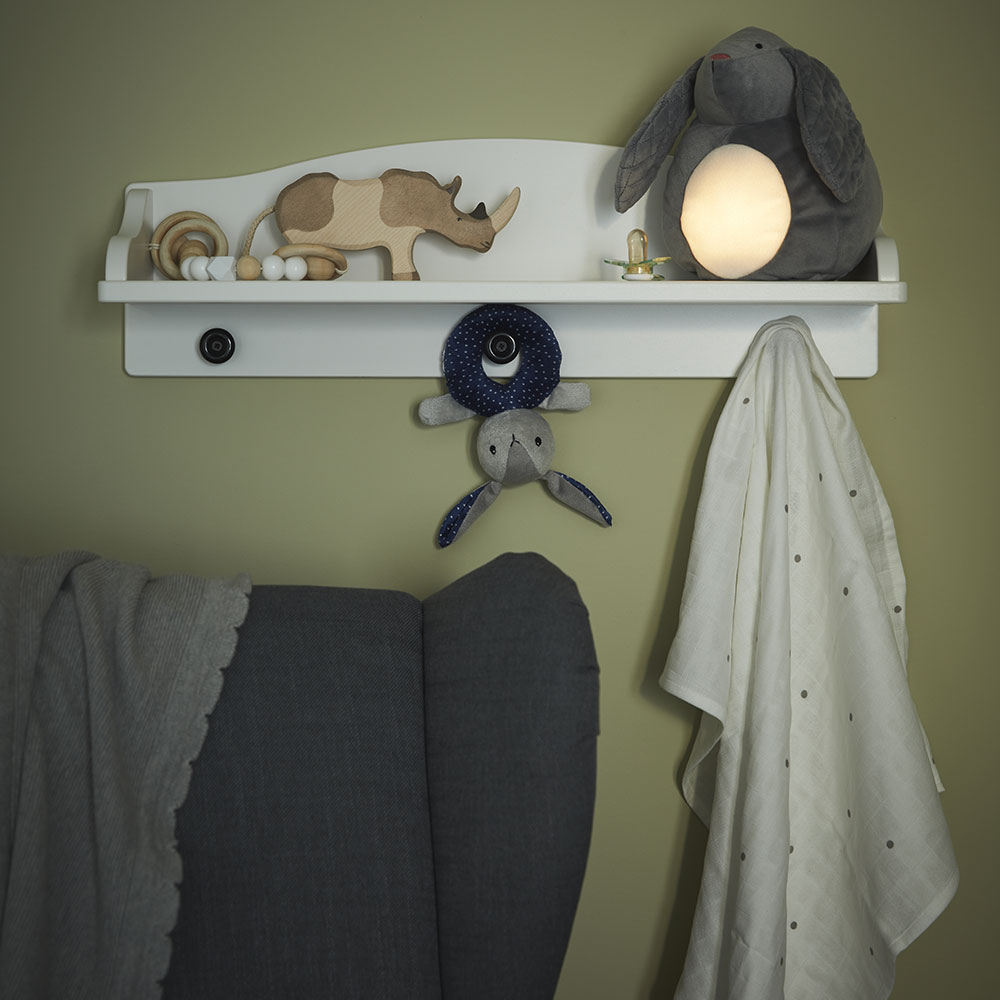 A GULLIGAST rattle placed on a wall shelf, a STRANDMON armchair with a LEN baby blanket.