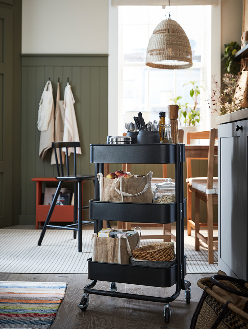 Utility trolley, black, vintage style, with glass and wood containers, jars and baskets on top.