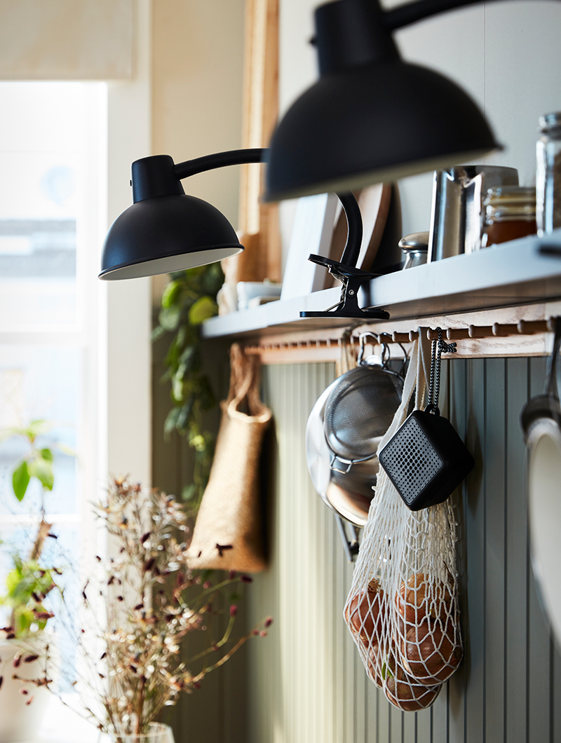 Clamp spotlight, there are shelves with glass jars and there is a rack with six knobs and has hung a mesh bag and a bluetooth speaker, in a vintage atmosphere.
