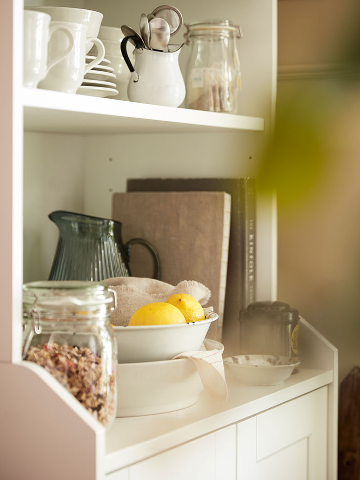 Detail of tall cabinet with shelves and lower doors, showing a jar with lid and fruit dishes.