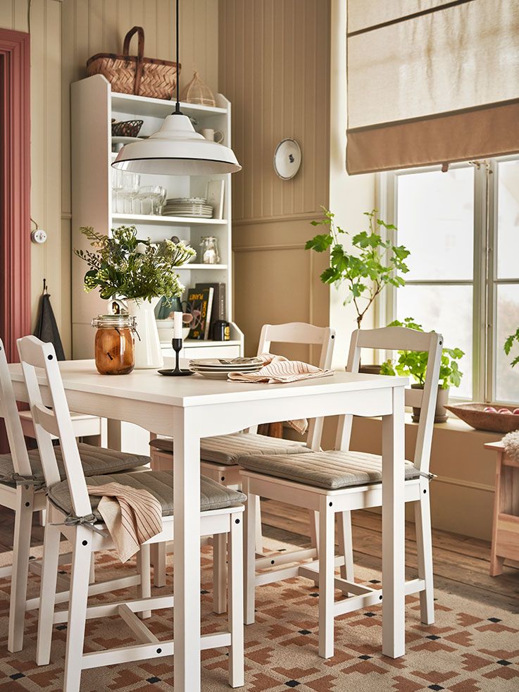 Traditional vintage style table and chairs in a dining room with a large window and a cupboard with vintage shelves.