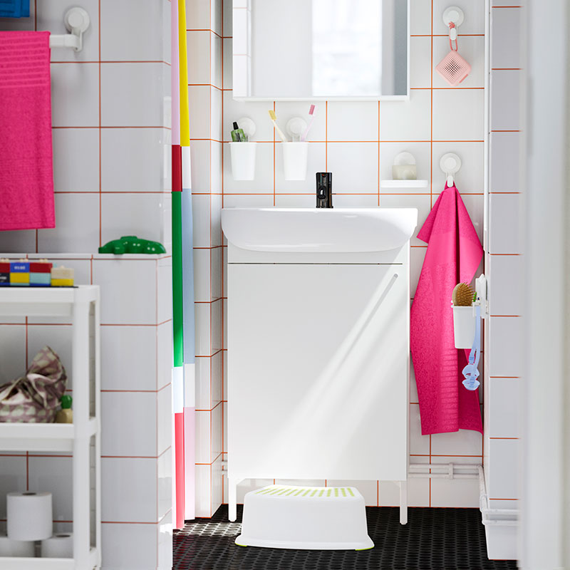  White bathroom with orange tiled grout. Pink towels, white step stool. Clean and functional atmosphere.