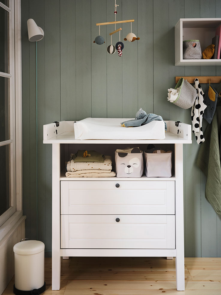 Dresser with white changing table, baby textiles around and a baby crib mobile hanging from the ceiling.