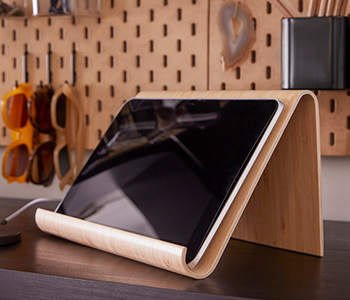 Tablet in wooden stand on dark desk with pegboard and sunglasses. Office.