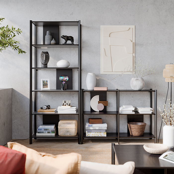 Una sala moderna con estanterías negras minimalistas llenas de libros, jarrones y objetos decorativos frente a una pared de concreto.