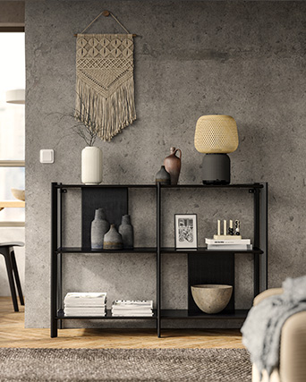 Aparador negro bajo con objetos decorativos sobre pared gris de estilo industrial.
