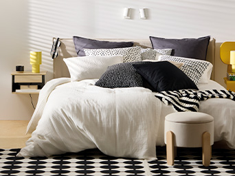 Dormitorio de IKEA decorado con textiles claros y oscuros, una alfombra y una lámpara de mesa amarilla