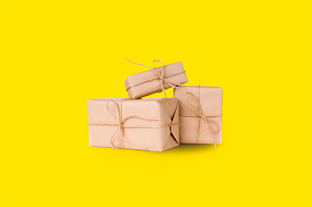 Tres regalos envueltos en papel kraft atados con cordel sobre un fondo amarillo.