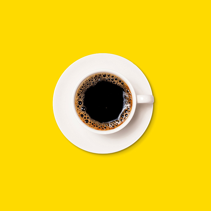 Taza de café negro con plato sobre un fondo amarillo, vista desde arriba.