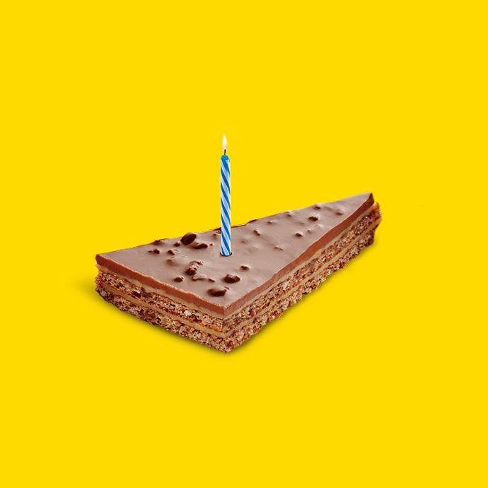 Porción de tarta de chocolate con una vela encendida sobre un fondo amarillo.