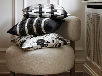 Three black and white graphic-patterned cushions stacked on a modern upholstered chair.