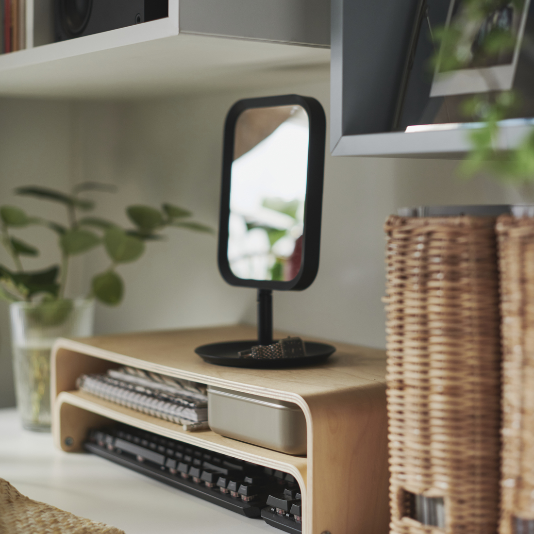 A workspace with a VATTENKAR laptop/monitor stand, a LINDBYN mirror above, accompanied by a basket and a book that bring style and organization to the space.