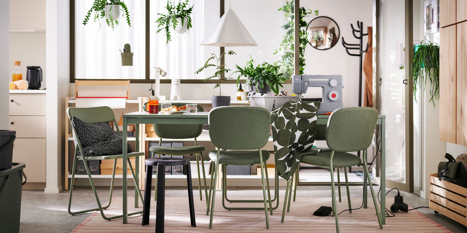 A bright, natural dining/workspace with green chairs, matching table, and plants.