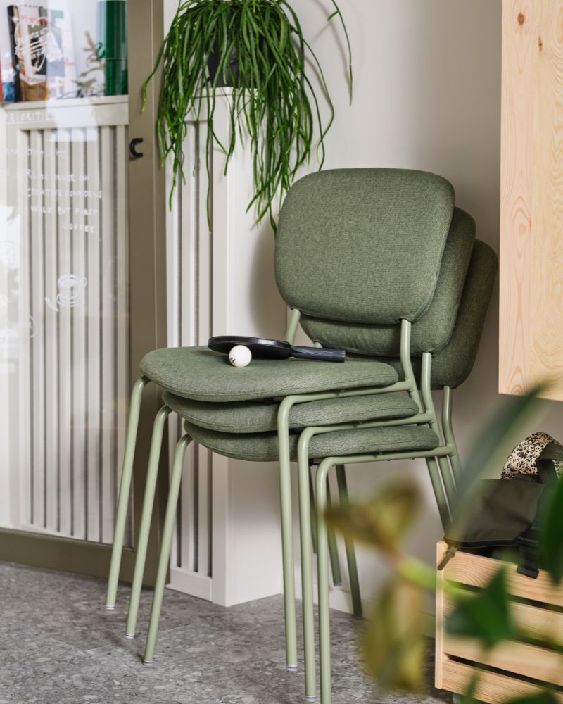 Stack of green chairs with a natural vibe, plants, and light wood furniture.