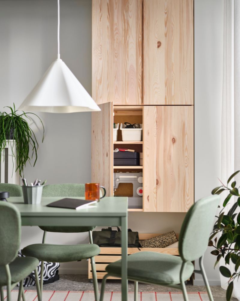 A light wood cabinet and green table with chairs, under a white pendant lamp. Functional ambiance.