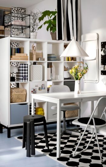 Room with white shelving unit, matching table and chairs. Bold patterned rug. Modern and functional ambiance.