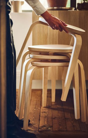 Stack of light wood stools, held by a hand. Natural and functional ambiance.
