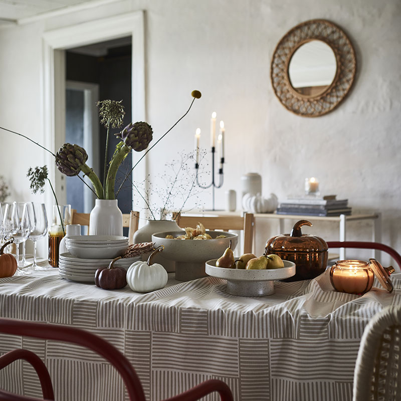 A light beige HÖSTAGILLE serving stand and bowl showcase fruit on a beautifully set dining table.