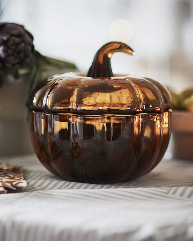 A close-up of the yellow-brown HÖSTAGILLE decorative bowl with a lid, featuring a pumpkin-shaped design on a patterned table