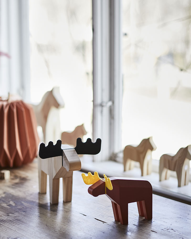 Two decorative HÖSTAGILLE moose figures are placed on a wooden table, surrounded by autumn decorations and natural light.