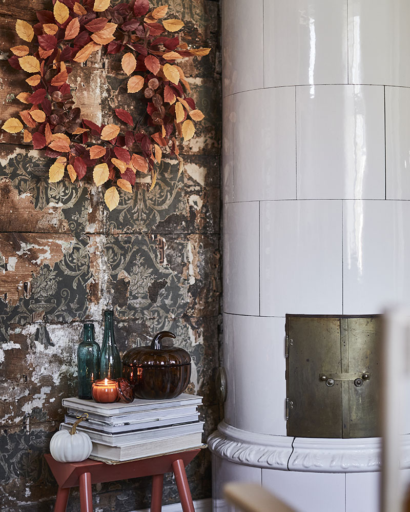 A HÖSTAGILLE artificial wreath in mixed colours adorns a rustic wall, set amidst decorative items, some books and a candle