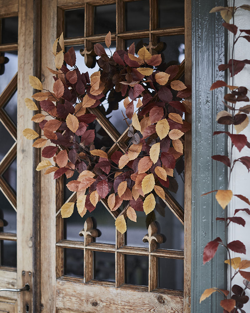 A wooden and glass door is adorned with a multicoloured HÖSTAGILLE artifi cial wreath in warm autumn hues
