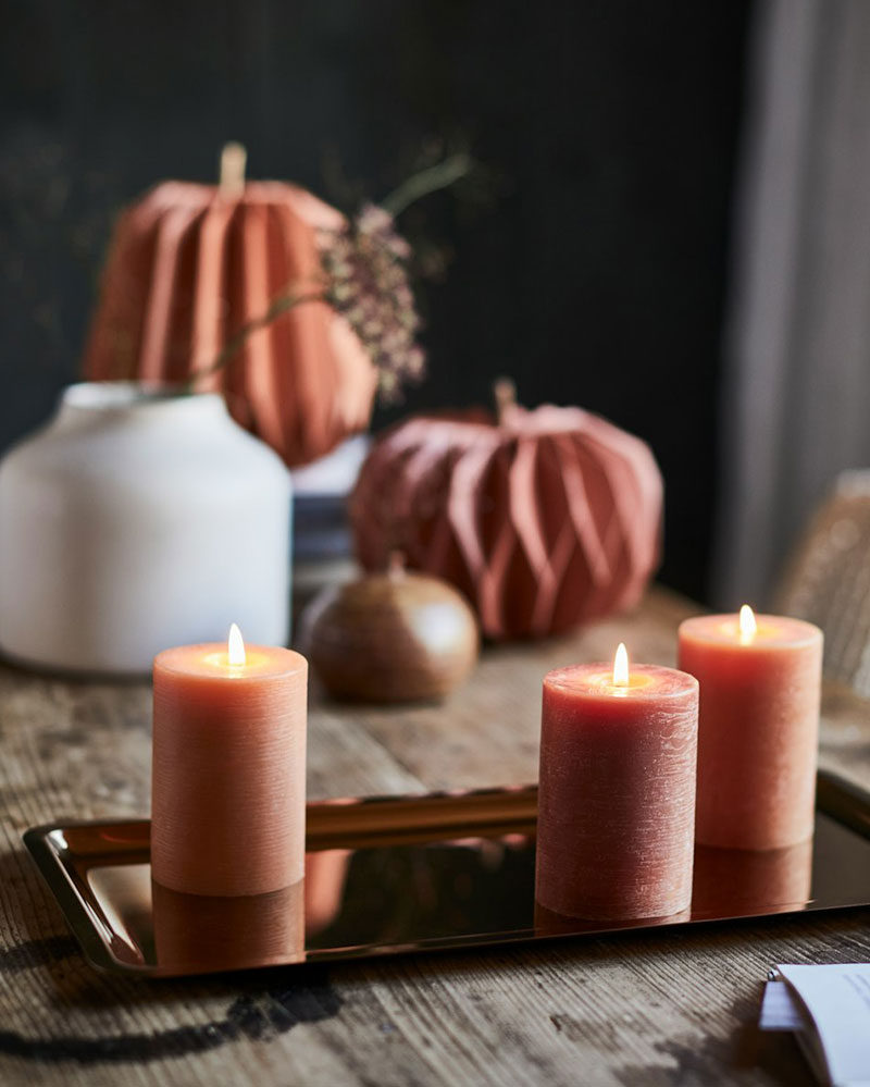 Three HÖSTAGILLE unscented pillar candles are placed on a shiny HÖSTAGILLE tray, surrounded by autumn decorations