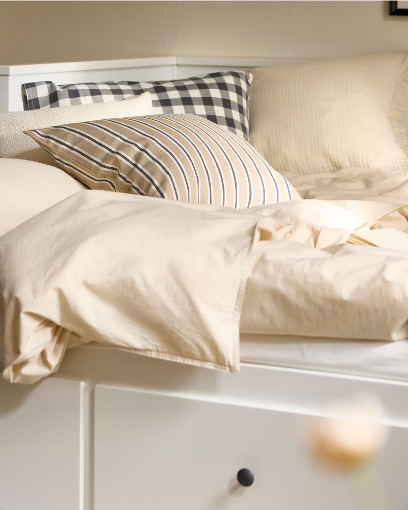 HEMNES day-bed made out as a double bed with undyed natural coloured ÄNGSLILJA bed linen on it and a striped cushion.
