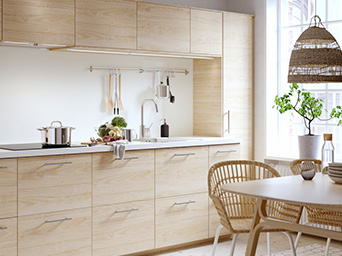 Cocina moderna de madera clara con encimera blanca, utensilios e iluminación natural.