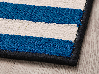 Primer plano de alfombra con rayas azules y blancas, con borde negro y textura tejida. Añade color y comodidad a tu espacio.