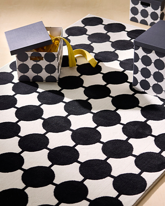 Alfombra blanca y negra con patrón de círculos, acompañada de cajas de almacenaje a juego. Organiza y decora tu hogar con soluciones inteligentes.