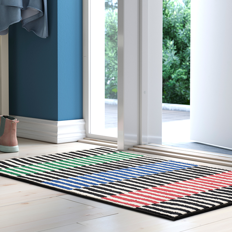 Felpudo multicolor de rayas asimétricas colocado en el vestíbulo de una casa luminosa