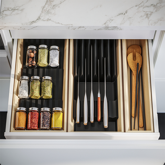 Cajón de cocina abierto mostrando organizadores para especias, cuchillos y utensilios de madera, manteniendo el contenido ordenado y accesible.