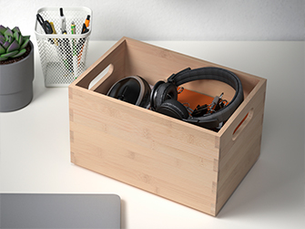 Caja de almacenamiento de bambú en un escritorio, conteniendo auriculares y pequeños accesorios, ayudando a mantener el área de trabajo ordenada.