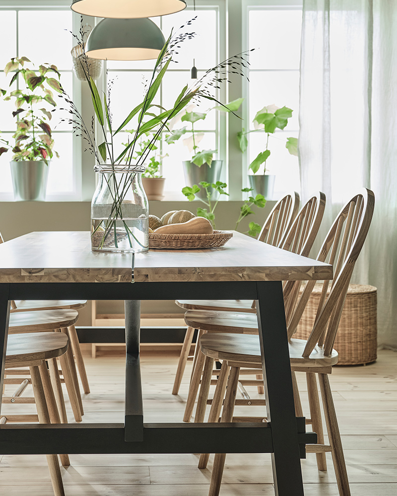 A SKOGSTA table with a BEGÄRLIG vase on top of it and several SKOGSTA chairs, two RÖDFLIK pendant lamps lighting the dining room.