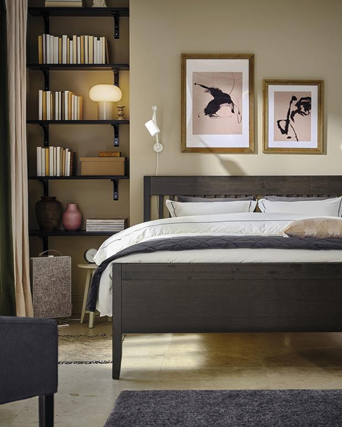 Dormitorio acogedor con cama de madera oscura, librería integrada y cuadros modernos.