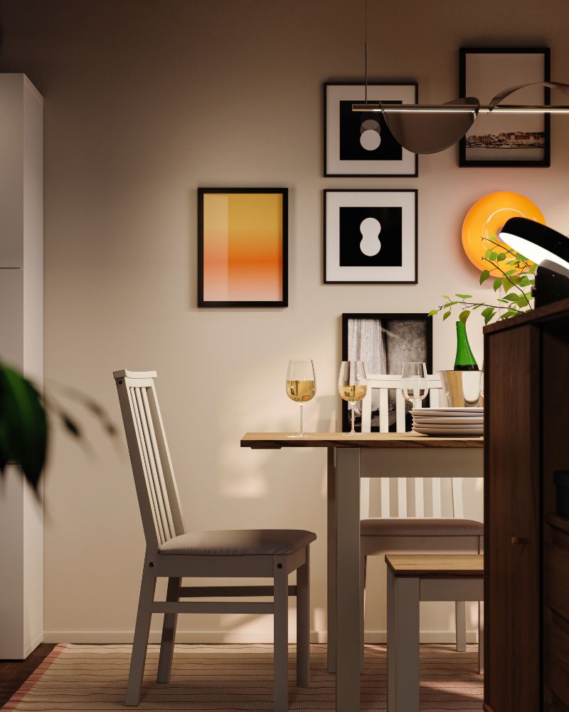 A dining area at night with an ÅLHULT dining set with an extendable table, a bench and chairs and a round, orange LED lamp.
