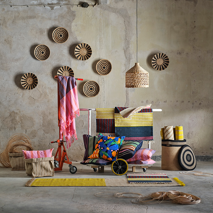 La colección MÄVINN está rodeada de paredes y suelo de concreto. Las fibras naturales se mezclan con textiles en rosa, azul y amarillo.