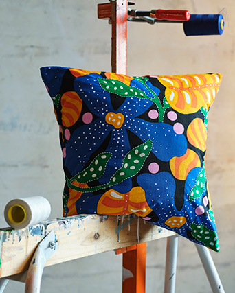 Una funda de cojín MÄVINN con un patrón floral multicolor descansa sobre una viga de madera manchada con pintura vieja.
