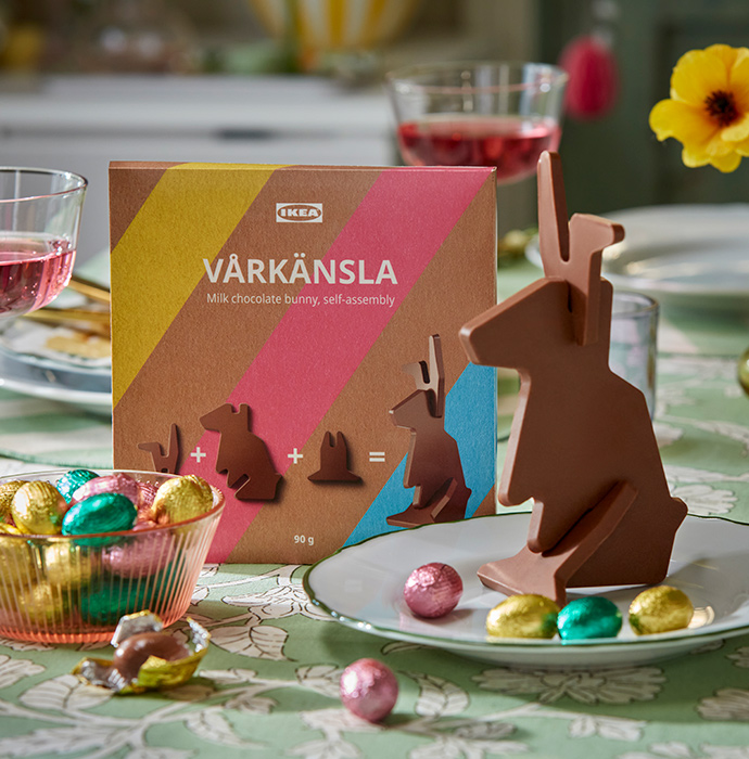 Un primer plano de un conejo de chocolate con leche VÅRKÄNSLA y algunos huevos de chocolate con leche VÅRKÄNSLA de colores, acomodados en un cuenco decorativo.