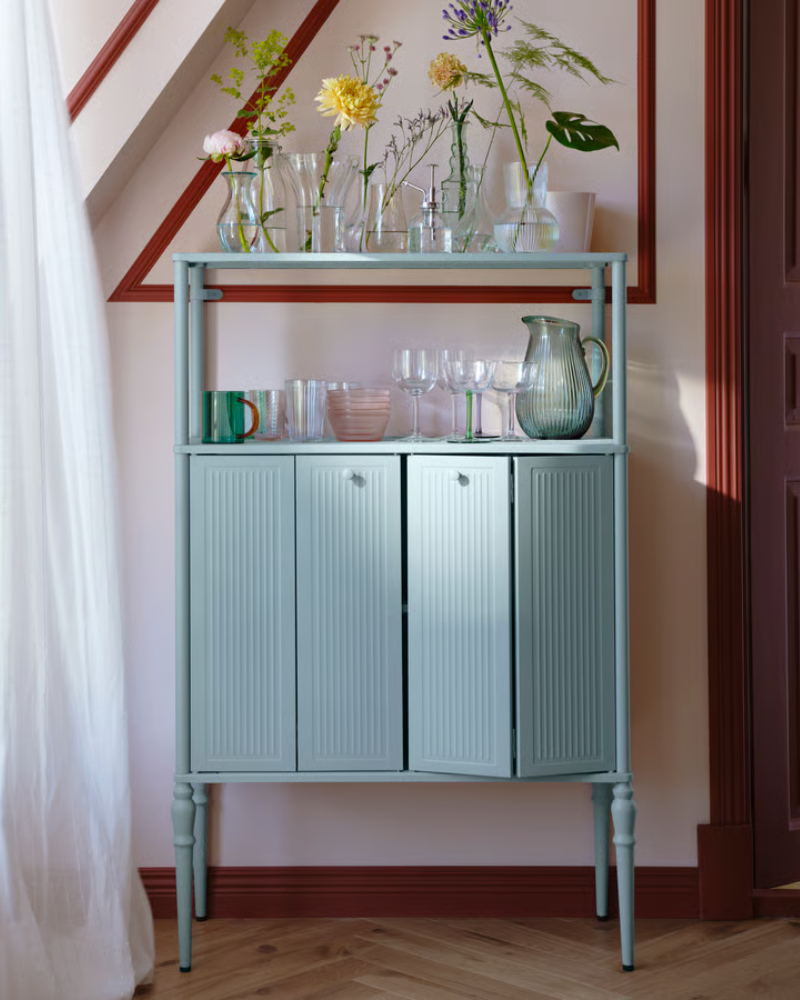 A light grey-blue SÅGMÄSTARE cabinet with glass jars and glasses on top, elegantly placed in a stylish interior.