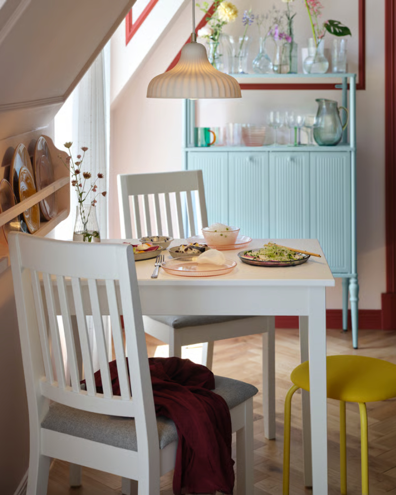 A white NÄSINGE table stands elegantly in a bright dining area with a light grey-blue SÅGMÄSTARE cabinet in the background.