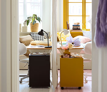 Dos escritorios BOLLPOJKE de pino/blanco uno al lado del otro en una habitación compartida,  con un lado decorado en tonos neutros y el otro más colorido.