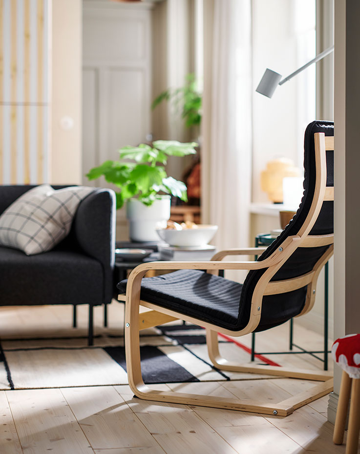 A bright living room with leafy plants and a black POÄNG armchair made with birch veneer, placed opposite a LILLEHEM sofa.