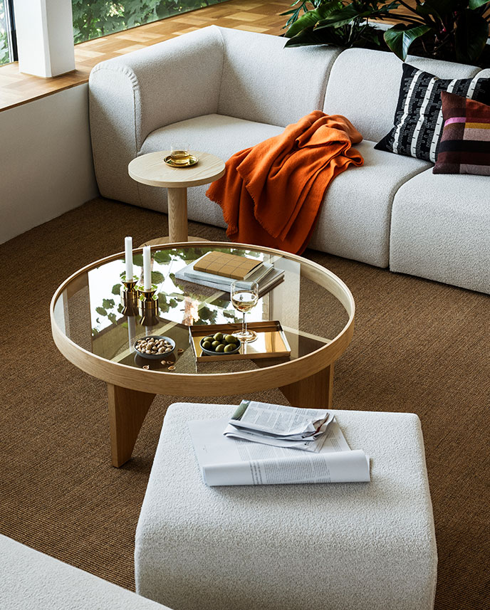 A living room with a green STOCKHOLM 2025 easy chair made of birch veneer with a woven seat, accompanied by a folded throw.